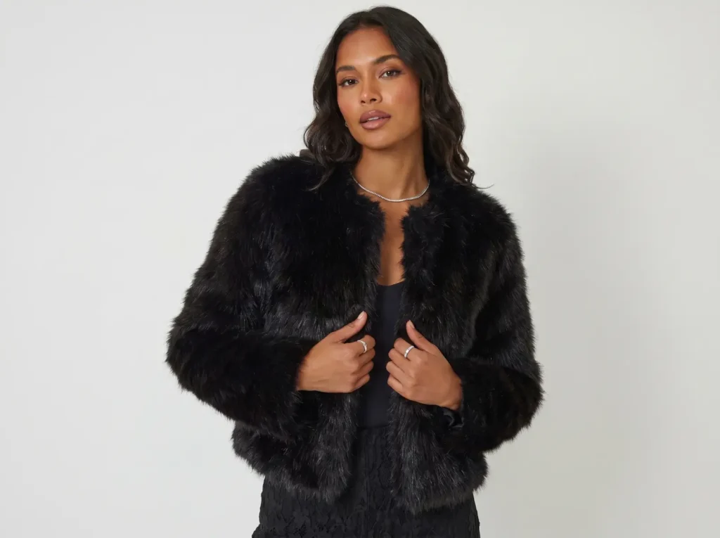 Mulher a usar casaco de pelo preto curto sintético para um look de inverno elegante e sem volume.